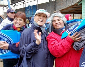 Aid recipients with their hands full smile alongside a Tzu Chi volunteer.
